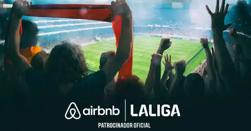 Airbnb y LaLiga: El Fichaje del Verano que Une Fútbol y Viajes. Logo de Airbnb y LaLiga en un estadio con fans celebrando, patrocinador oficial de La Liga.